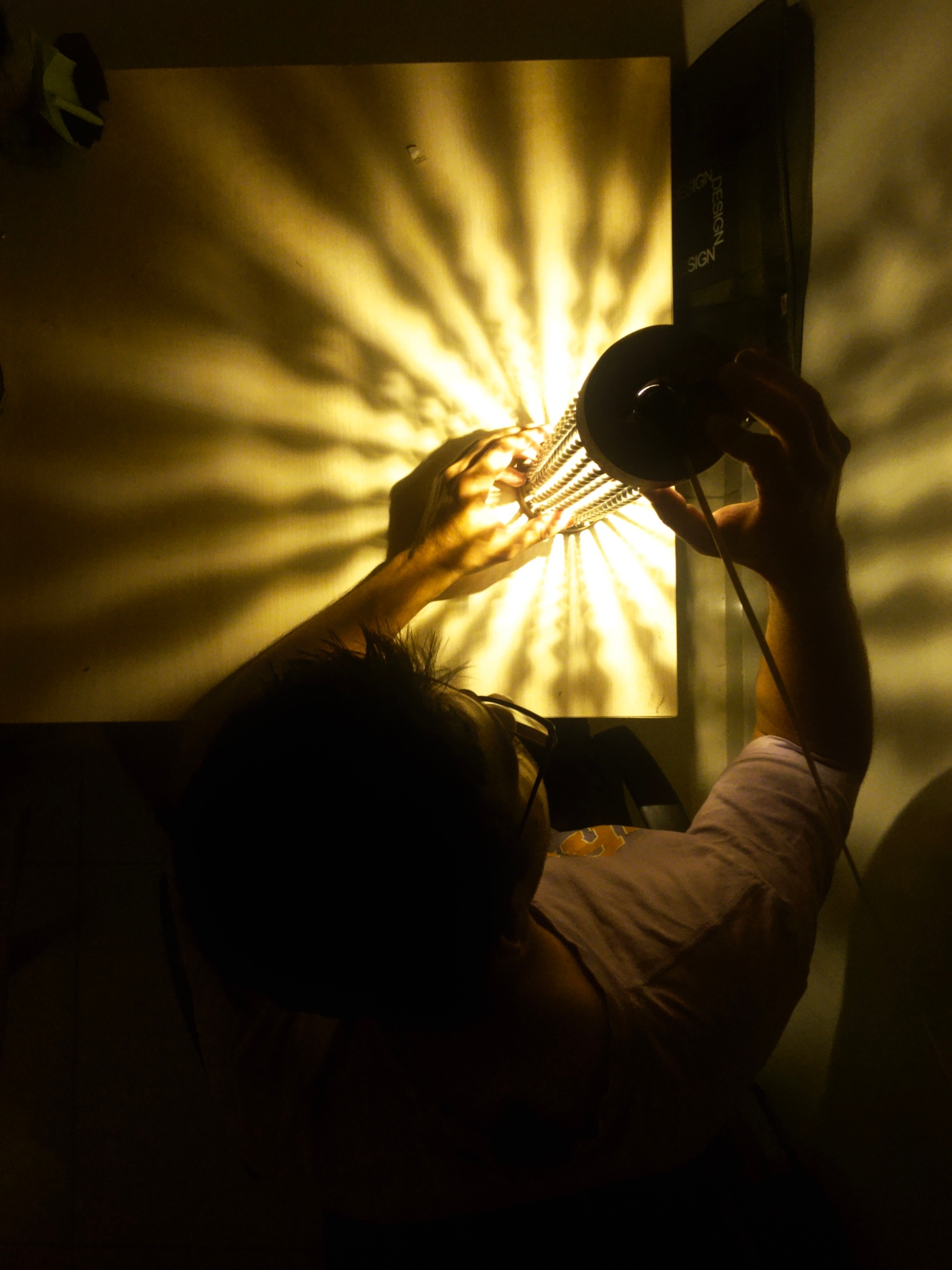 Hand positioning the lamp as shadows spread across the wall